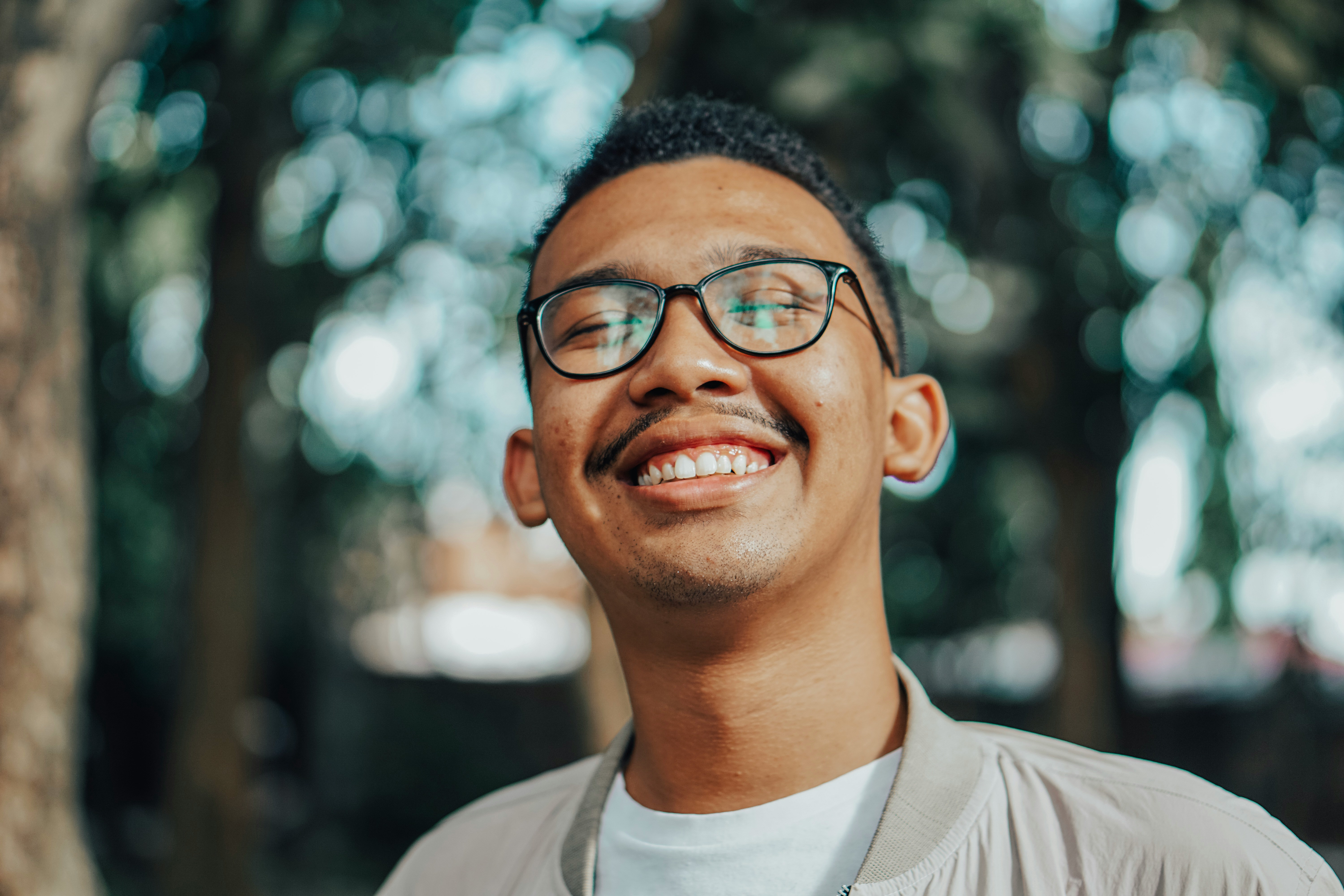 Smiling person in glasses outdoors with trees in background